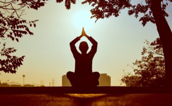 Silhouette of a person practicing yoga outdoors during sunrise, creating a calming atmosphere.