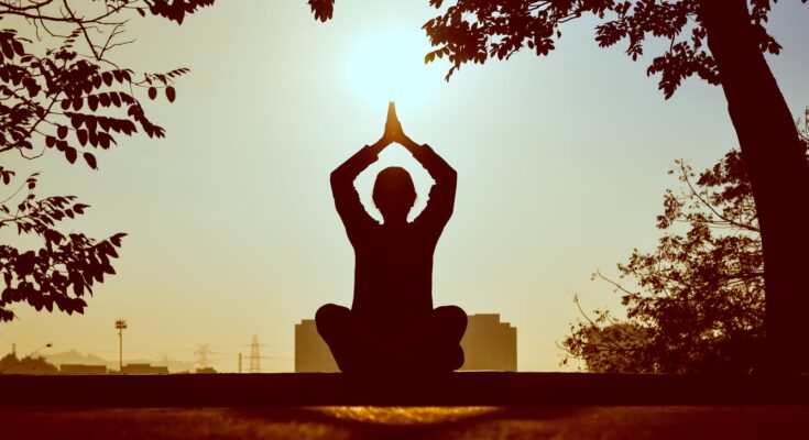 Silhouette of a person practicing yoga outdoors during sunrise, creating a calming atmosphere.