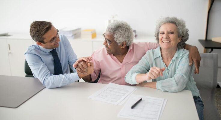 Senior couple in office meeting with consultant, discussing financial documents and smiling.